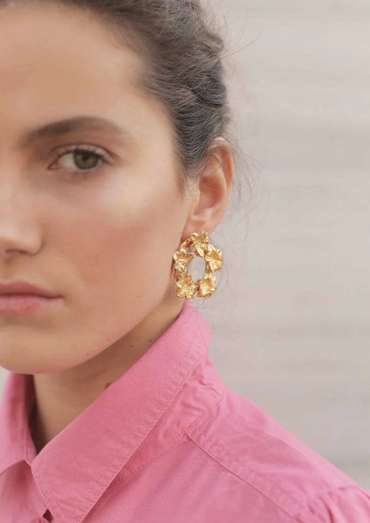 Mujer con blusa rosa usando pendiente dorado en forma de aro con flores, estilo elegante.