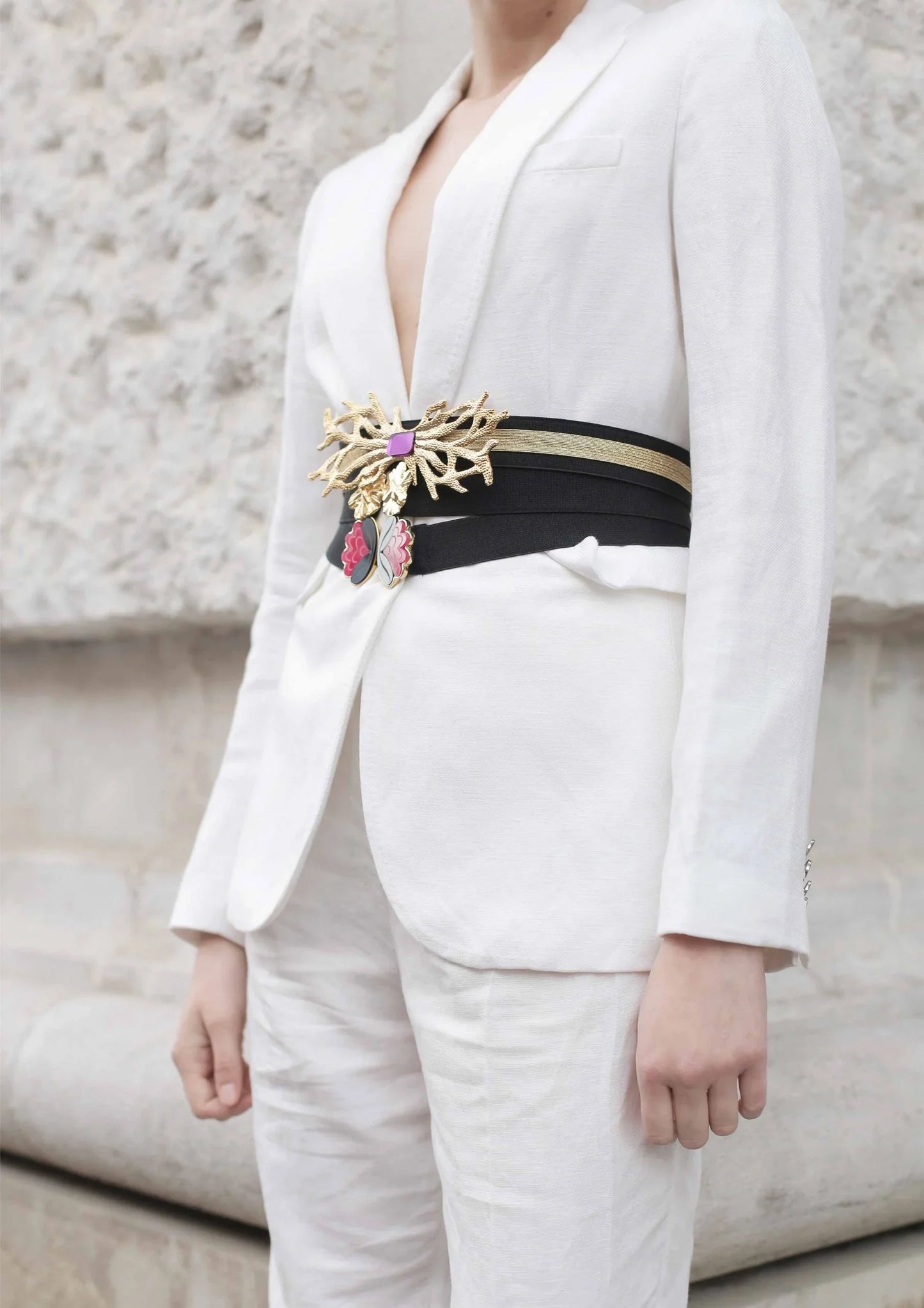 Cinturón elegante negro con adorno dorado y rosa sobre traje blanco femenino