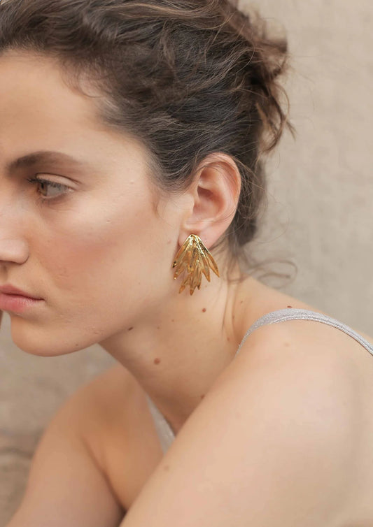 Mujer luciendo pendiente dorado grande de diseño artístico, fondo neutro