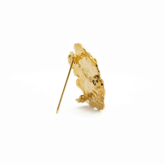 Broche dorado texturizado, forma irregular, sobre fondo blanco, accesorio de moda elegante
