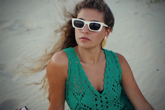 Mujer con gafas de sol blancas y vestido verde de crochet en playa, moda verano