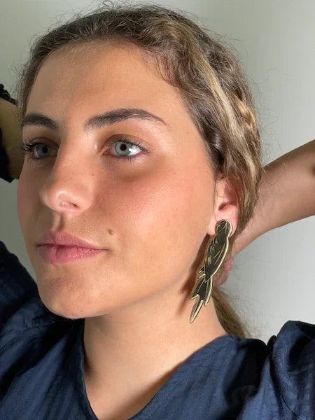 Mujer luciendo pendiente grande dorado de diseño artístico, fondo neutro, estilo moderno