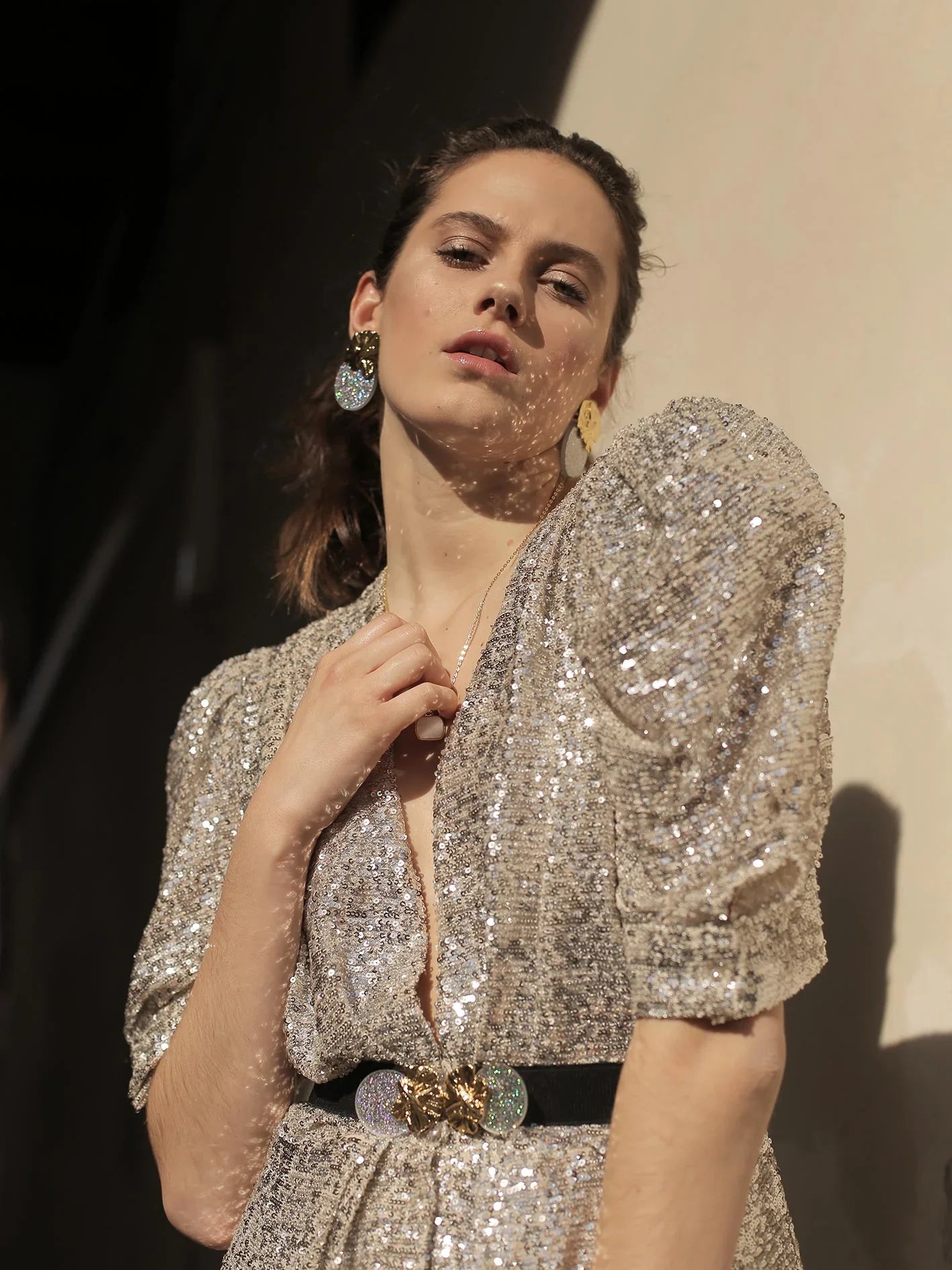 Mujer con vestido de lentejuelas doradas y cinturón elegante, pendientes brillantes, luz natural.
