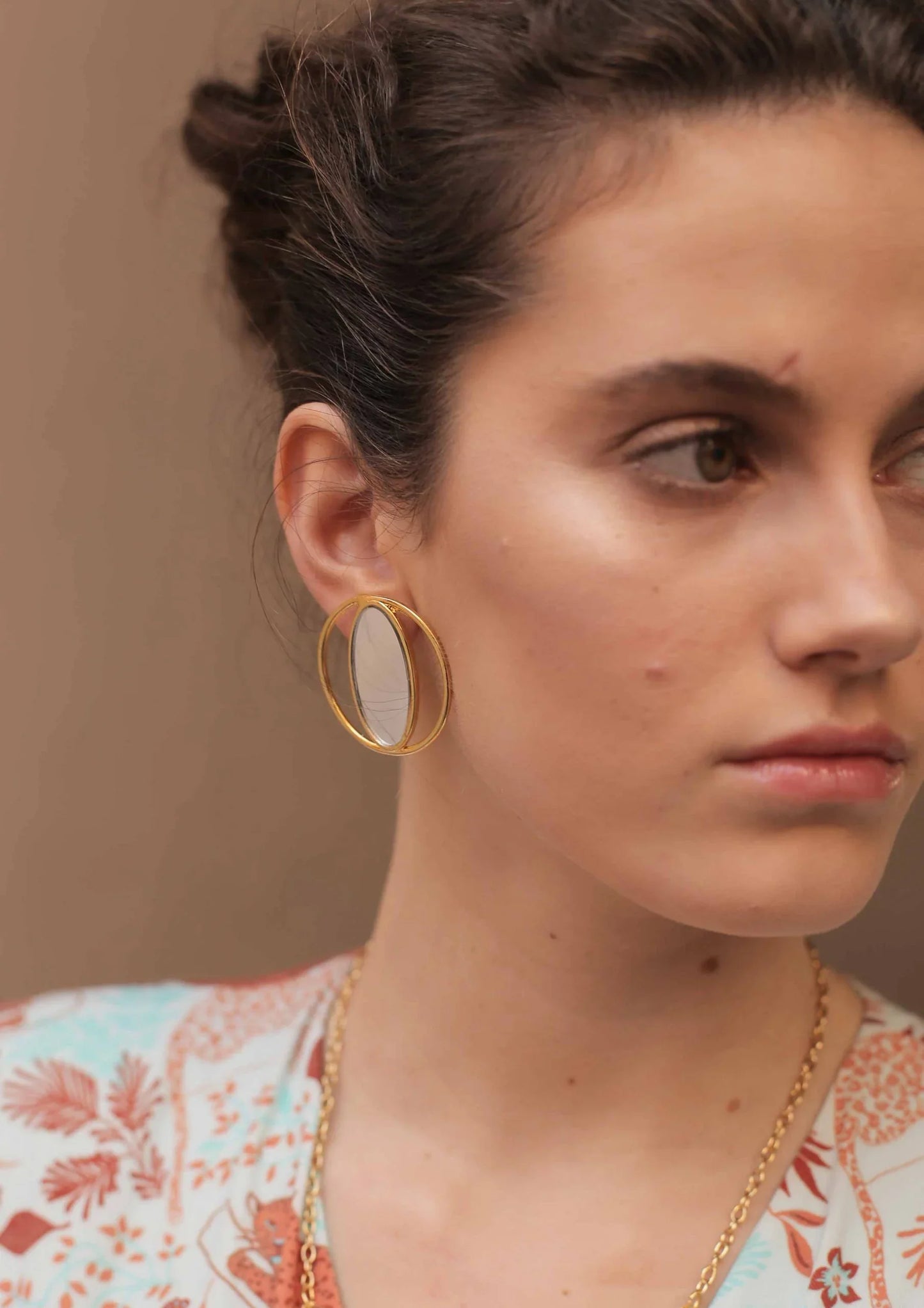 Mujer luciendo pendiente ovalado dorado moderno, fondo neutro, estilo elegante