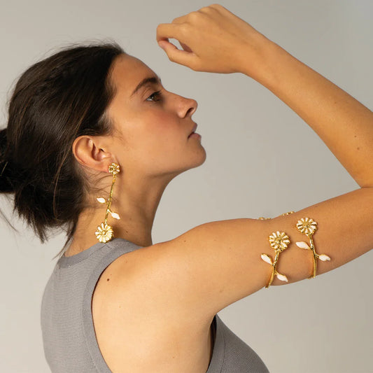Mujer luciendo pendientes y brazalete dorados con diseño de girasol blanco, estilo elegante.
