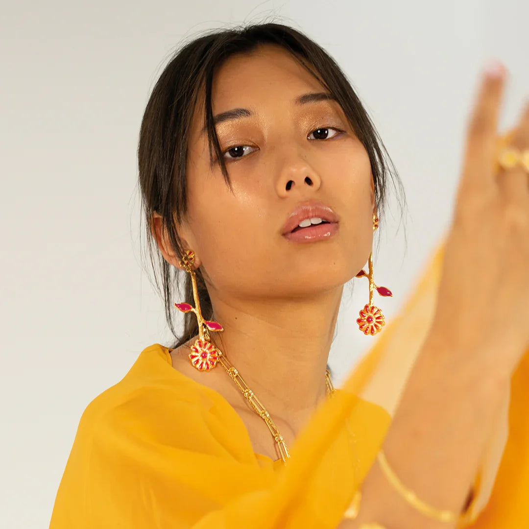 Mujer luciendo pendientes girasol esmaltados en rojo y dorado, estilo elegante.
