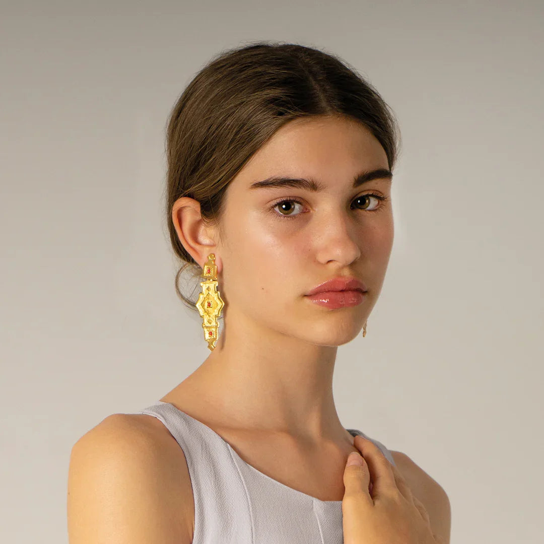 Pendientes largos dorados con detalles en rojo coral, modelo mujer elegante