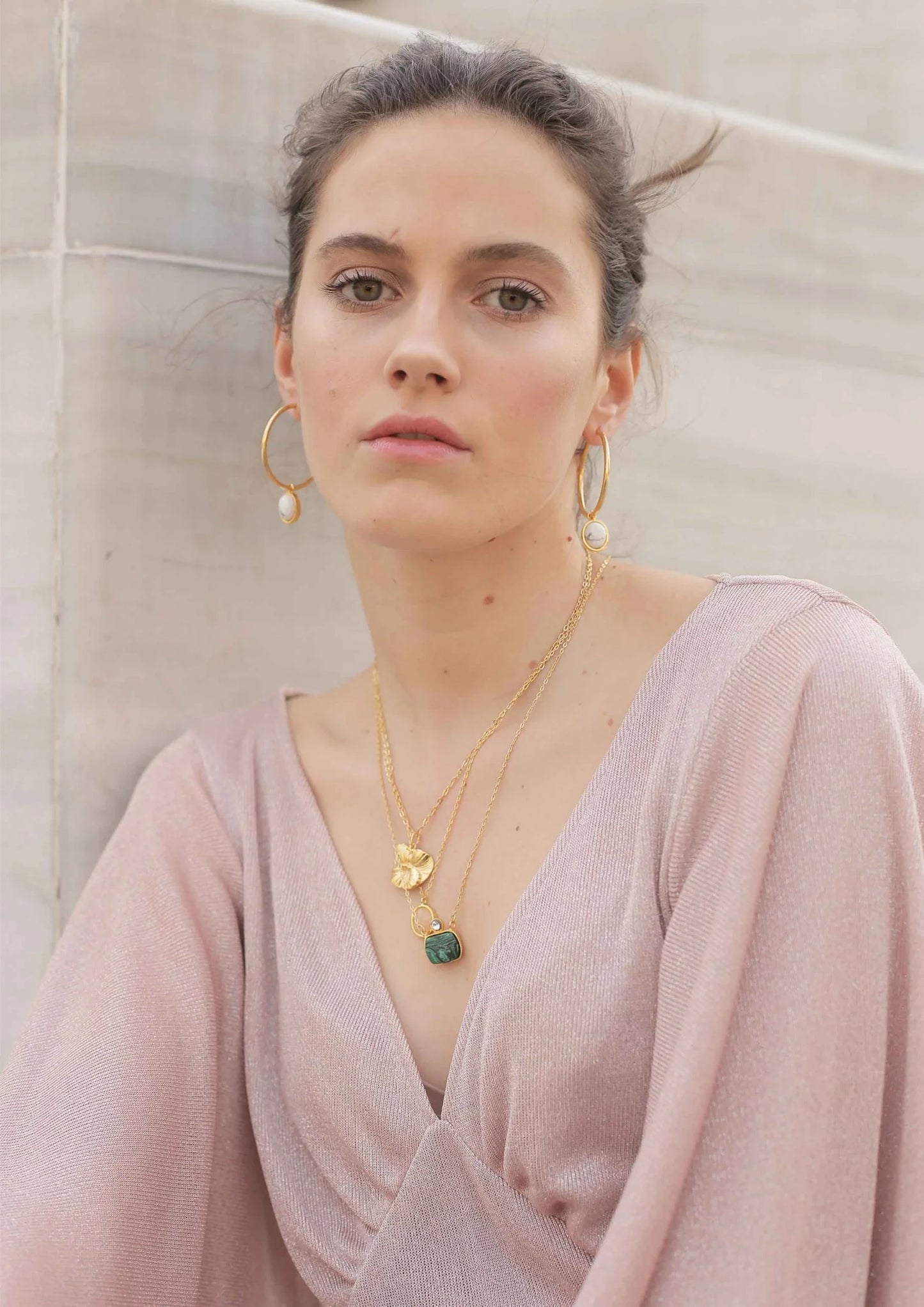 Mujer con pendientes dorados y colgantes de oro y piedra, fondo de mármol elegante.