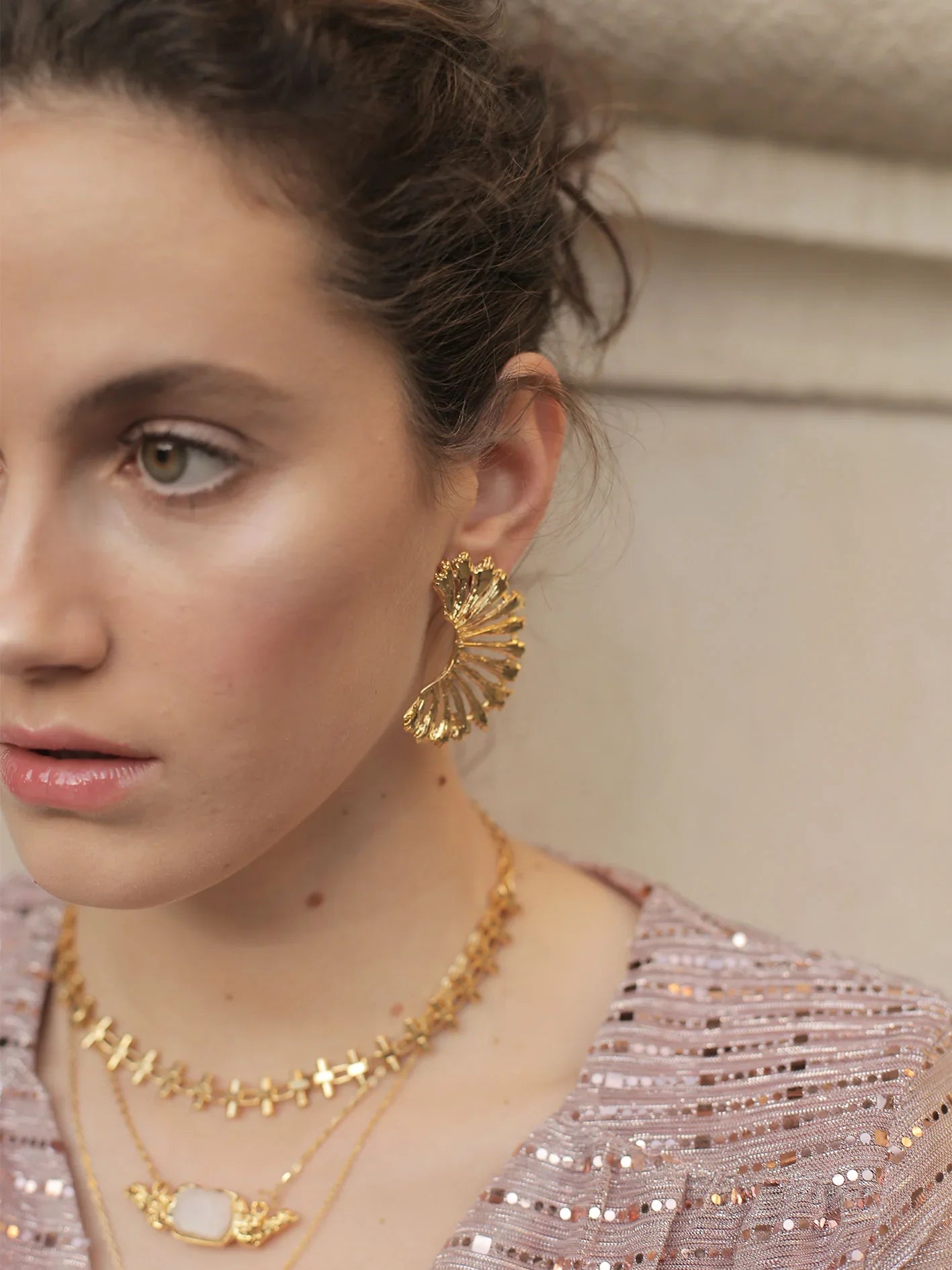 Mujer con pendientes dorados grandes en forma de anémona y collares dorados elegantes
